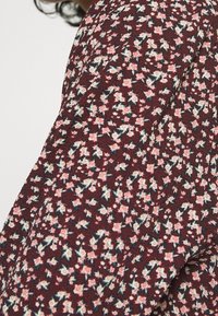 Gros plan d'un tissu bordeaux avec une texture froissée, présentant un motif dense de petites fleurs roses et blanches avec des feuilles vertes.