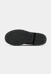 Black rubber shoe sole with a textured pattern, featuring ridges for grip and a logo imprinted on the middle section.