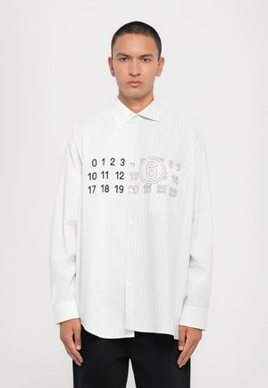 Chemise blanche à boutons avec une moitié à rayures contrastantes et des chiffres imprimés sur le côté uni. Elle présente un col classique et des manches longues.