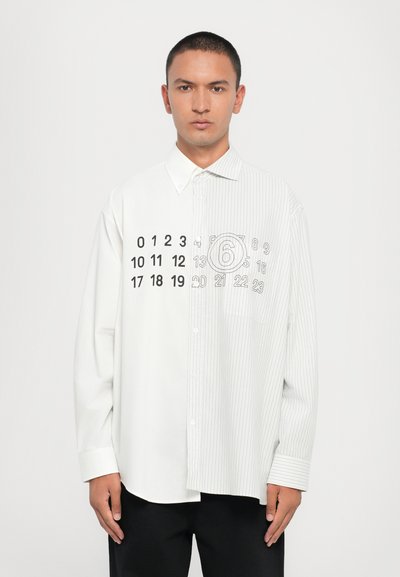 Camisa blanca de botones con medio lado de rayas en contraste y números impresos en el lado sólido. Presenta collar estándar y mangas largas.