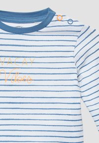 Wit en blauw gestreepte blouse met lange mouwen en de tekst "Vacay Vibes" in oranje, en blauwe drukknoopjes op de schouder.