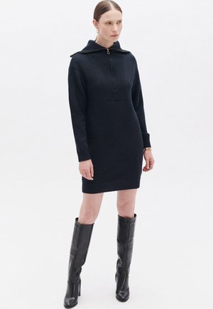 Vestito lavorato a maglia blu navy con collo alto e chiusura con zip; presenta maniche lunghe e orlo a coste. Abbinato a stivali neri al ginocchio.