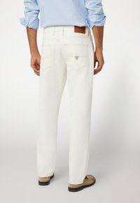 Balti džinsai su tiesiomis kojomis. Yra užpakalinės kišenės ir tekstūruota ruda odinė etikete ant liemens.