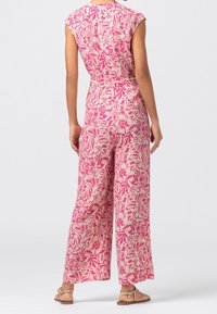 Rosa blommig jumpsuit med korta ärmar, vida ben och en mjuk tygkvalitet som har ett upprepande bladmönster.