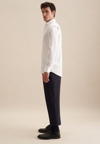 Witte lange mouwen shirt gecombineerd met marineblauwe broeken en zwarte schoenen. Het shirt heeft een klassieke kraag, terwijl de broeken een rechte snit hebben.