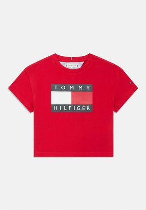 Červený krátký crop top s krátkými rukávy a logem Tommy Hilfiger, zobrazujícím bílý, červený a modrý obdélníkový design vlajky uprostřed na hrudi.