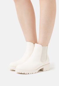 Botines blancos con un exterior de cuero suave, paneles laterales elásticos y una suela gruesa con relieve, que presentan un diseño minimalista.