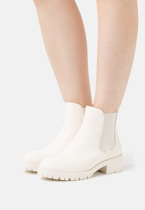 Bottines blanches à cheville avec un extérieur en cuir lisse, des panneaux latéraux élastiques et une semelle épaisse à relief, présentant un design minimaliste.