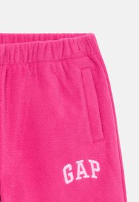 Fleece trenirke v svetlo roza barvi z elastičnim pasom in stranskimi žepi. Na sprednji strani je izvezen logotip "GAP" v beli barvi.