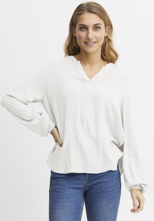 Vit långärmad blus med V-ringning, texturerad tyg och elastiska manschetter. Matchad med blå jeans. Har en avslappnad passform och sidokilar.