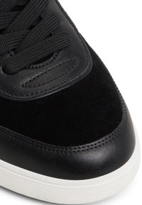 Czarny sneakers z połączeniem gładkiej skóry i teksturowanego zamszu. Posiada białą gumową podeszwę i czarne sznurówki. Klasyczny design.