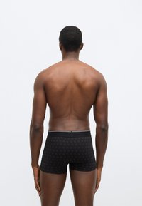 Fekete boxeralsó, finoman ismétlődő mintával, fehér szegéllyel ellátott rugalmas derékrésszel, puha anyagból készült, testhezálló kialakítás.