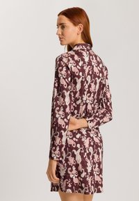 Dlouhý rukáv šaty v burgundské barvě s paisley vzorem v růžové a bílé, s límcem a volným střihem, který sahá až do poloviny stehen.