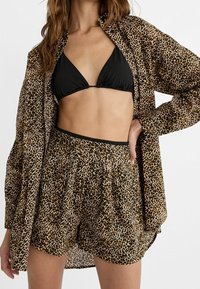 Košile s leopardím potiskem, černý bikinový top a odpovídající šortky. Materiál vypadá lehký, s elastickým pasem a volným střihem.