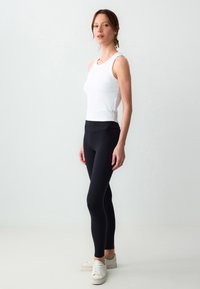 Top bianco a costine e leggings neri a vita alta. I leggings hanno una texture liscia, abbinati a scarpe da ginnastica bianche con suola bassa.