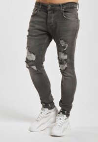 Grå denimjeans med revne lapper på knærne, slim fit, og en lett falmet struktur. Kombinert med hvite atletiske joggesko.