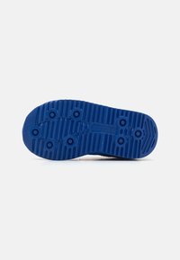 Semelle de chaussure en caoutchouc texturé bleu avec un motif de rainures et de grips circulaires. Détail de marque notable en relief sur la surface.