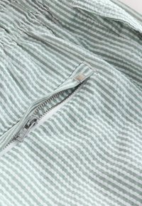 Light green and white striped fabric with a smooth texture, featuring a silver zipper with a rectangular pull tab and a branded tag.