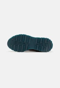Suela de zapato de goma con un agarre texturizado, de color azul claro con surcos y patrones distintos, marcada con "bugatti".