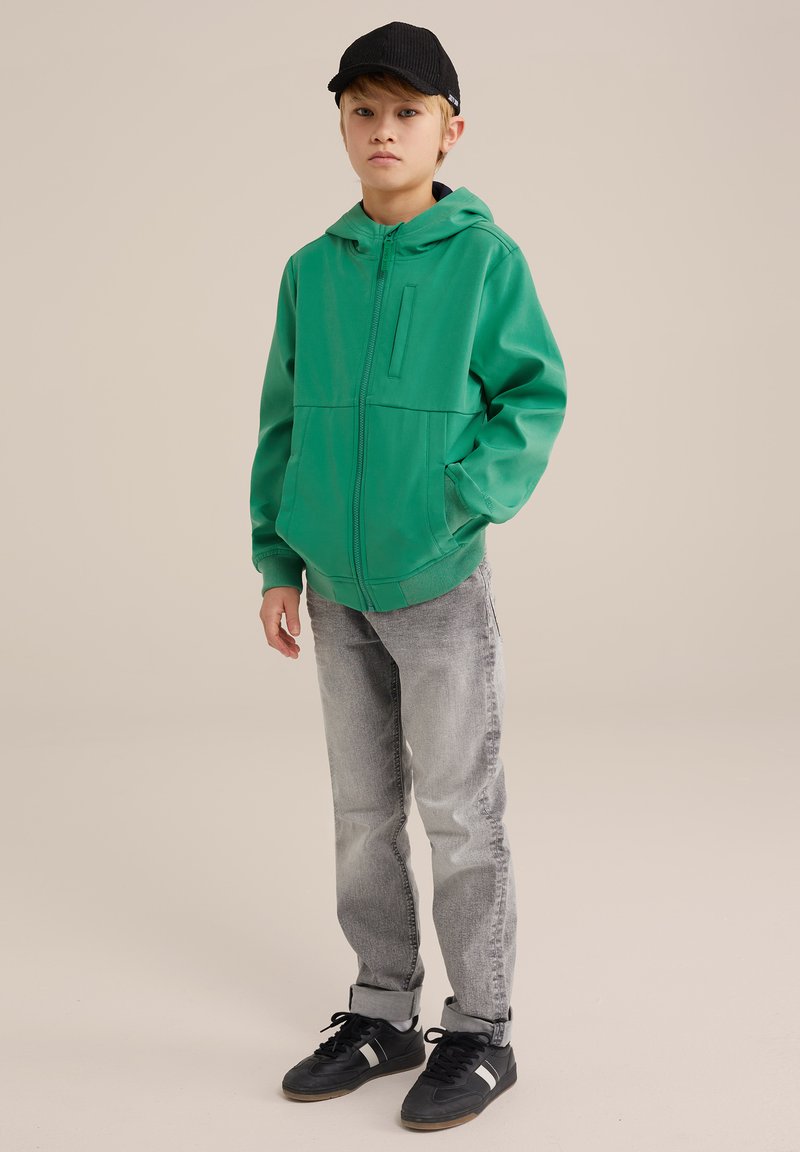 Felpa verde con zip, dotata di tasca frontale, jeans grigi e sneakers nere. La felpa presenta un cappuccio e una tasca a marsupio per un look casual.
