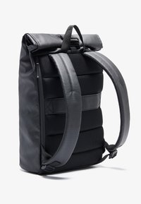 Czarny plecak z rolowanym zamknięciem, z wyściełanymi siateczkowymi paskami, gładką fakturą i kieszenią na zamek. Posiada elegancki, minimalistyczny design.