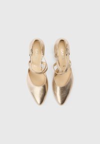 Talons métalliques dorés avec un bout pointu et une bride à la cheville, présentant une texture lisse et un design minimaliste.