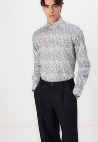 Cămașă cu mâneci lungi, cu un model floral albastru și maro, confecționată dintr-un material ușor; asociată cu pantaloni bleumarin, cu un nasture în față și plieri.