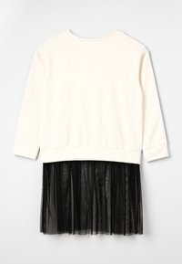 Top de mangas largas en color crema combinado con una falda de tul negro con pliegues. El top tiene un escote redondo y un dobladillo acanalado. Contrastes de textura entre las telas.