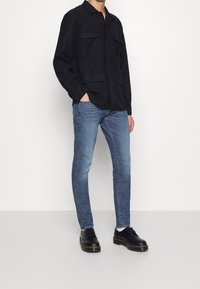 Svart, långärmad skjorta med knappar och två bröstfickor, kombinerad med ljusblå slim fit-jeans och svarta snörstövlar med tjock sula.