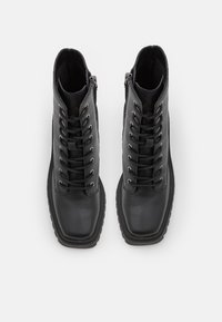 Paire de bottes en cuir noir à lacets avec bouts carrés et fermetures éclair latérales, vues de dessus sur fond blanc.