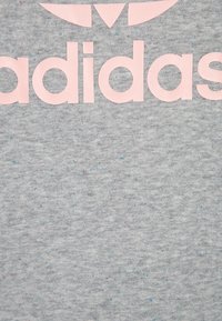 Ljusgrå sweatshirt med en mjuk textur, med en stor rosa "adidas"-logotyp över bröstet och små färgfläckar i hela tyget.