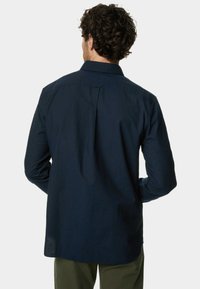 Camisa de botones en azul marino con mangas largas, un cuello clásico y un pliegue en la parte posterior; fabricada con tejido tejido de textura suave.