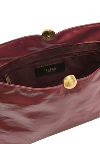 Bolso de piel burdeos con una textura suave, herrajes dorados y un bolsillo con cremallera. El interior cuenta con un forro de tela y una etiqueta de marca.