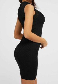 Robe sans manches en tricot noir avec un motif texturé, silhouette ajustée et longueur au-dessus du genou, mettant en valeur une finition lisse et des coutures latérales.