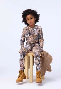 Patterned pajama set featuring various animal faces in shades of brown and cream, paired with yellow boots, sitting on a wooden stool.