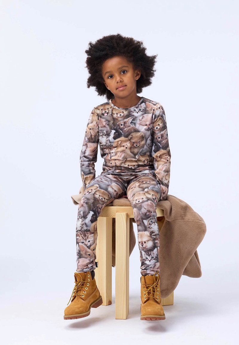 Patterned pajama set featuring various animal faces in shades of brown and cream, paired with yellow boots, sitting on a wooden stool.