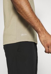 Camiseta Dri-FIT color caqui de manga corta, con detalle de etiqueta en la cintura, combinada con pantalones cortos negros. Tejido texturizado, corte ajustado.