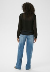 Doorzichtig zwart blouse met sneeuwvlokken, lange mouwen en elastische manchetten, gecombineerd met lichtblauwe wijde jeans met zichtbare zakken.