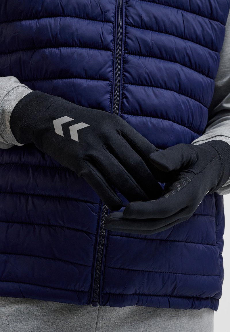 Schwarze Handschuhe aus flexiblem Material, mit einem schlanken Design, strukturierten Griffen und silbernen Pfeilmustern auf der Rückseite.