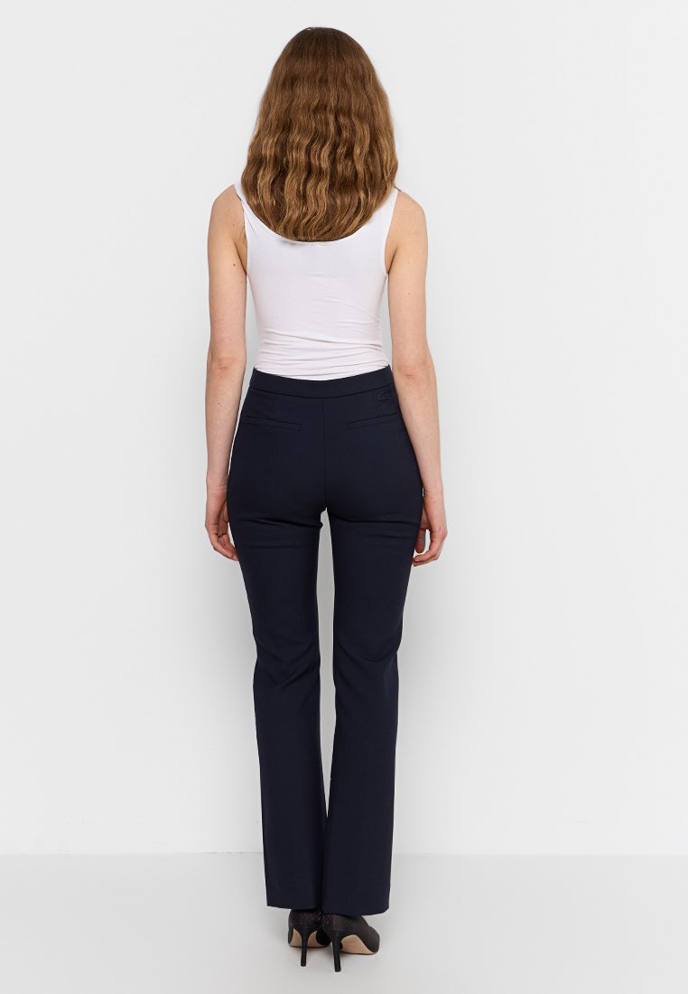 Pantalon ajusté bleu marine foncé, doté de poches arrière et d'une texture de tissu lisse. Porté avec un débardeur blanc.