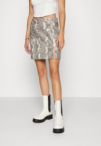 Mini-jupe à motif serpent en argent et beige, avec une fente latérale. Portée avec des bottines blanches ornées d'accents noirs sur les côtés.