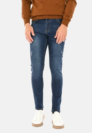 Jeans in denim skinny-fit di colore blu scuro, con leggera usura, design a cinque tasche e vita media. Abbinati a sneakers bianche.
