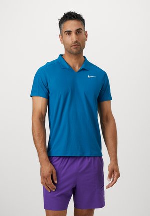Turkis Nike polo skjorte med kort krave og korte ærmer. Har et lille hvidt logo på brystet. Bæres med lilla shorts.