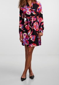 Robe à imprimé floral en noir avec des nuances de rose, rouge et bleu. Manches longues, encolure boutonnée, taille cintrée et jupe fluide.
