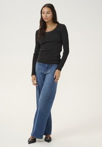 Black long-sleeve top with a scalloped neckline, paired with wide-leg blue jeans. The outfit features a fitted style with a textured fabric.