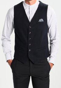 Schwarze formelle Weste aus glattem Stoff mit schmalem Revers, sechs Knöpfen, zwei Fronttaschen und einem dekorativen Einstecktuch.