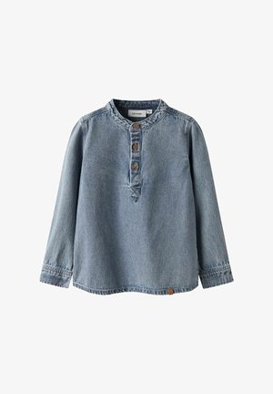 Hele sinise teksariidest pikkade varrukatega särk ümarate kraega, viie nupuga lõhikuga ja väikese logoga äärisel. Näha on kulunud tekstuur.