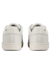 Ett par vita låga sneakers med vadderade kragar, synlig sömnad och "G-STAR RAW" präglat på hälarna, visade från baksidan.