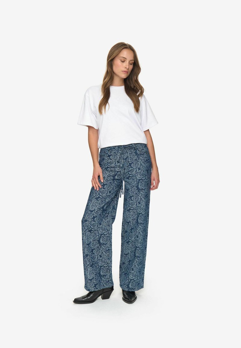 Blå blommönstrade vida byxor med dragsko i midjan, i kombination med en vit t-shirt med kort ärm och svarta ankelboots.