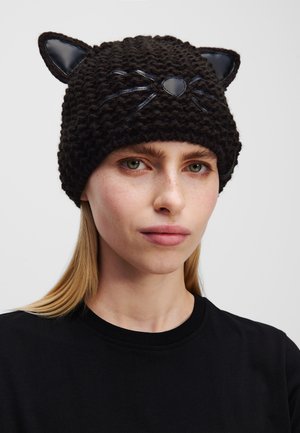 Gorro negro de punto con orejas de gato, que presenta acentos negros brillantes para los bigotes y la nariz. Textura suave, forma redondeada y diseño ajustado.